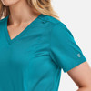 A women's double v-neck top in teal, featuring short sleeves and a logo on the sleeve.