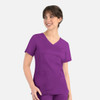 A purple curved mock wrap top with short sleeves and pockets, worn by a smiling model.