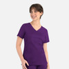 A women's curved mock wrap top in a rich purple colour, featuring short sleeves and two front pockets.