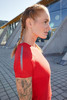 A red ladies sports T-shirt is displayed on a model with braided hair and a tattooed arm. The shirt features reflective accents.