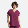 A woman models a deep burgundy women's top with a v-neck and short sleeves, featuring a front pocket.