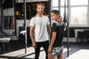 A ladies' sports shirt in black with a patterned back, worn by a model alongside a man in a white t-shirt.