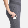 A pair of grey flare leg pants with a full elastic band, featuring a pocket on the side, showcasing a hand placing an item inside.
