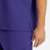 A close-up of a purple men's v-neck top featuring a side split and a hand holding it. The fabric appears smooth.