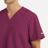 A men's v-neck top in a deep burgundy colour with a chest pocket and shoulder detail, featuring a logo.