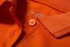 An orange sleeveless polo shirt featuring a collar and a button, with a logo label inside.