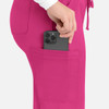 A close-up of bright pink cargo pants with a phone being placed into a back pocket. The pants feature a logo.