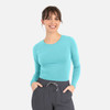 A woman wearing a teal long-sleeve underscrub tee with a rounded neckline, paired with grey pants.