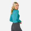 A woman wearing a teal long-sleeve underscrub tee and grey pants, showcasing the back view of the top.