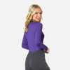 A woman smiles while wearing a long-sleeve, purple underscrub tee with a grey bottom. The tee has a logo.