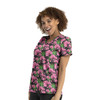 A woman smiles while wearing a vibrant pink floral V-neck print top against a black background. The top features a floral pattern.