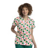 A woman wearing a short-sleeve, pink V-neck top with a festive print of Christmas trees, snowmen, and decorations.