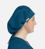 A unisex bouffant cap in deep teal, featuring a logo, worn by a model showcasing its profile.