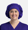 A unisex bouffant cap in purple, worn by a person with a smiling expression, featuring a soft, gathered design.