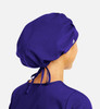 A unisex bouffant scrub cap in vibrant purple, featuring a logo and ties at the back.