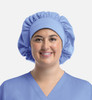 A unisex bouffant scrub cap in light blue, featuring a gathered design and soft fabric, worn by a smiling person.
