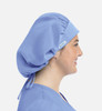 A unisex bouffant cap in light blue, featuring a gathered design and a logo. In use by a person, side profile view.