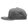 A grey camo snapback cap with a structured high profile and a patterned brim, featuring a logo.
