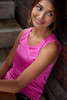 A pink ladies active tank top worn by a woman sitting on steps with wooden background. The top features a logo.