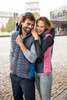 A knitted hybrid vest in navy with blue and pink accents, worn by a smiling couple outdoors. The vest has a hood and a logo.