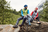 A green and blue knitted fleece vest is worn by a man, while a red vest adorns a woman. Both are outdoors in nature.