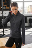 A black half-zip ladies sports shirt with long sleeves, featuring a logo, displayed in a gym setting.