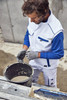 A man in a white and blue workwear softshell vest mixes material in a bucket on a construction site.