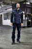 A padded work vest in navy blue with light blue accents, featuring pockets and a logo, worn by a person indoors.