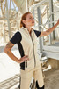 A woman wearing a cream and navy fleece vest, standing in an industrial setting with visible machinery in the background.