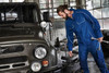 A blue workwear softshell jacket is being worn by a man fixing a vehicle in an industrial setting.