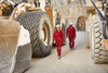 Two workers in red overalls and helmets walk between large machinery in a quarry setting.