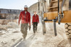 Two individuals wearing red polar fleece jackets walking in a quarry, with heavy machinery in the background.