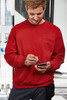 A red men's round sweat pocket jumper displayed on a man using a smartphone, featuring a logo on the chest.
