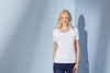 A white ladies' t-shirt with a round neckline and short sleeves, modelled by a woman against a blue background.