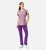 A woman wearing a floral v-neck print top in purple and pink, paired with purple pants. The outfit includes a logo.