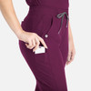 A pair of tapered leg pants in burgundy, featuring side pockets and a logo, with a hand placing a card into a pocket.
