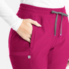 A close-up of pink Embrace Nora bootcut pants featuring an elastic waistband and side pockets. The pants have a logo.