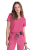 A pink medical top with a V-neck design, paired with matching scrubs. The model is accessorised with a small device.