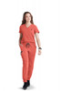 A woman in an orange scrub set walks confidently, featuring a V-neck top and drawstring pants. The outfit includes a logo.