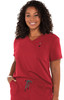 A woman wearing a red scrub top with a V-neck and a pocket, featuring a small logo on the chest.
