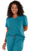 A woman in a teal scrub top with a v-neck and a chest pocket, smiling and standing with hands behind her back.