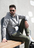 A grey hoodie jacket sits on a man lounging on a wooden bench, wearing green pants and sunglasses.