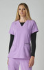 A lavender scrub top with short sleeves, featuring two front pockets. The model is wearing a black long-sleeve top underneath.