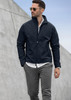 A man wearing a navy soft shell jacket and grey trousers, with sunglasses and a white shirt underneath.