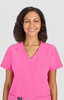A woman smiles while wearing a bright pink scrub top. The top has short sleeves and a v-neck design.