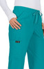 A pair of teal scrubs with a drawstring waist and pockets, featuring a logo on the side.