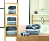 A selection of grey and white guest towels neatly folded on a wooden shelf and a countertop, with a towel set beside a bathtub.