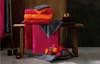 A stack of vibrant towels in pink, orange, and grey arranged on a wooden bench, with candles nearby.