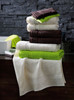 A stacked arrangement of towels in white, brown, and green, with varying sizes and textures, placed on a dark surface.