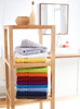 A display of neatly stacked bath towels in various colours, including grey, yellow, red, and blue, on a wooden shelf.